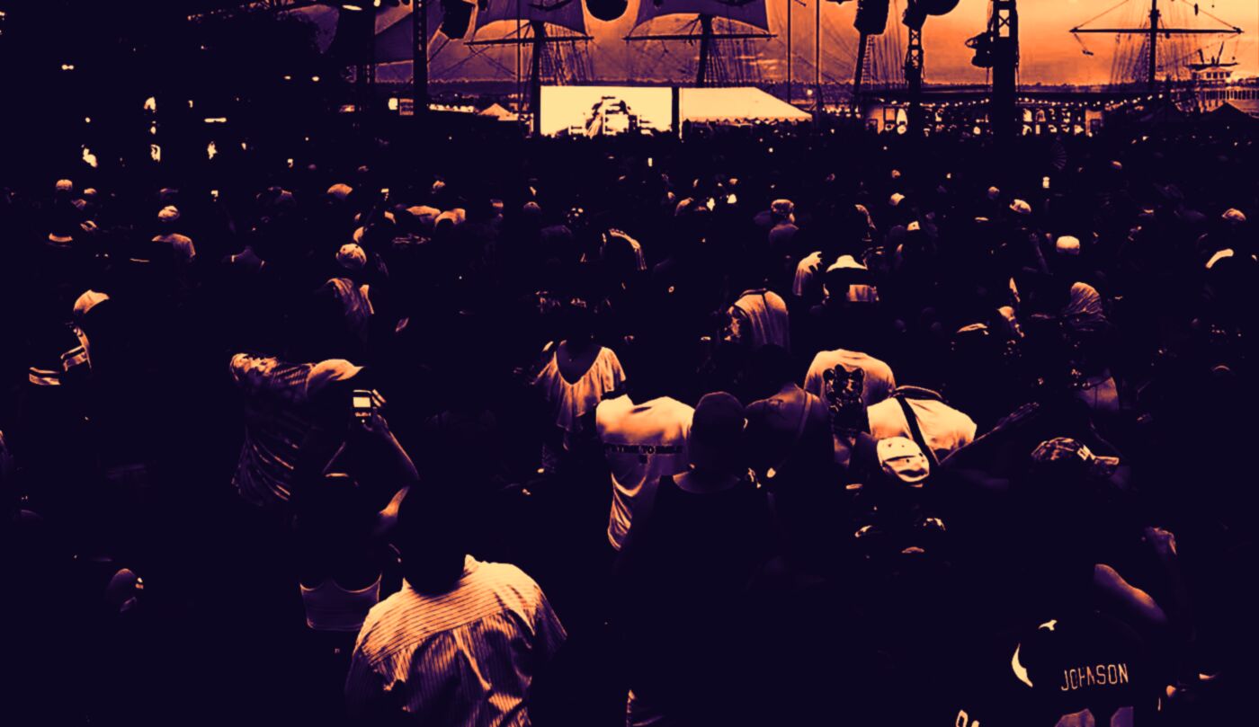 Silhouetted crowd dancing at a waterfront stage at sunset