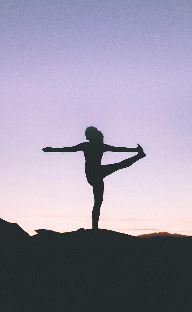 Silhouette balancing in a yoga pose on a ridge at dusk